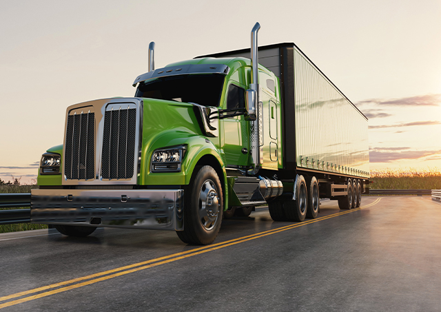 A green semi truck driving on a highway during sunset.