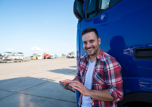 A professional truck driver standing by his truck holding his phone