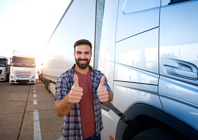 Professional truck driver beside his truck, smiling and giving a thumbs-up