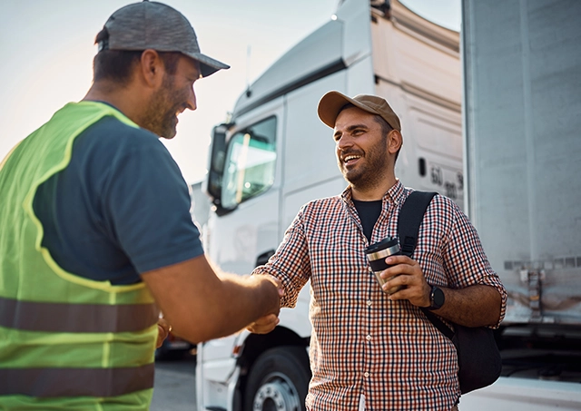 Truck refinance options accessed by a happy driver shaking hands with a transport worker in front of a white commercial semi-truck