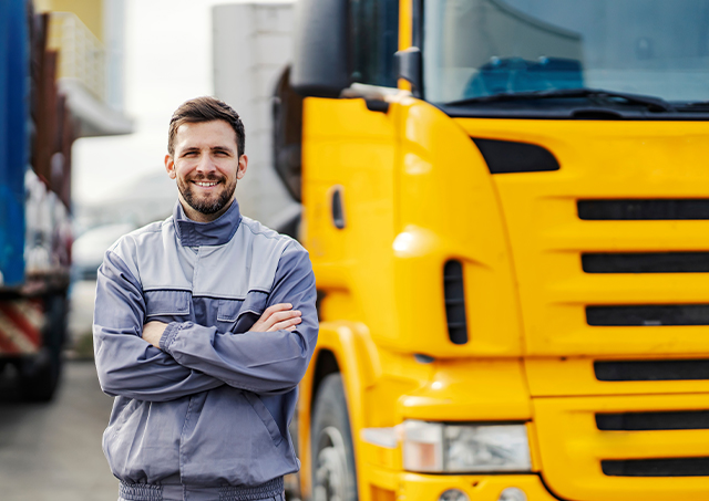 Commercial trailer financing options utilised by a smiling driver in a grey jumper standing in front of a yellow transport truck