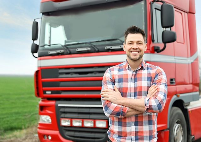 Competitive truck refinance solutions accessed by a smiling driver standing with arms crossed in front of his red semi-truck