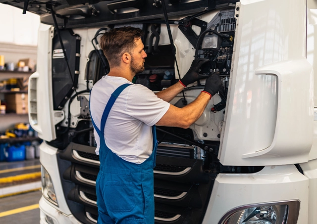 Truck repair loans accessed to fund mechanical maintenance on a white semi-truck engine by a technician in blue overalls