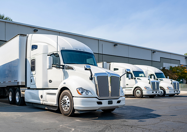 Rent to own truck loan vehicle ownership options for white high-cab long-haul semi-trucks lined up at warehouse docks