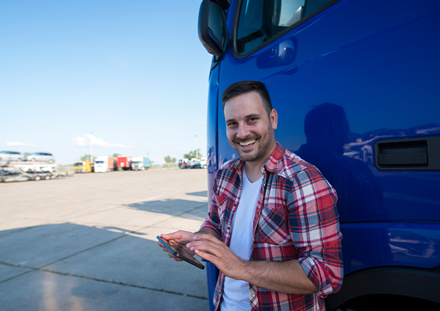 Professional truck driver standing by his truck, using a tablet.