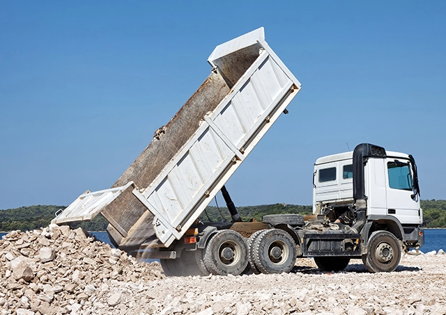 Tipper truck unloading crushed rocks at a construction site.