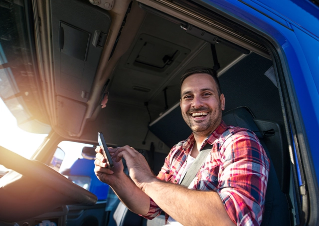 Truck loan interest rates compared on a smartphone by a happy driver in a plaid shirt inside a blue truck cabin