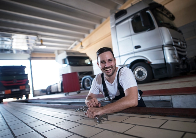 Commercial truck repair loans sourced to cover maintenance costs, featuring a happy mechanic holding a spanner inside a garage service pit