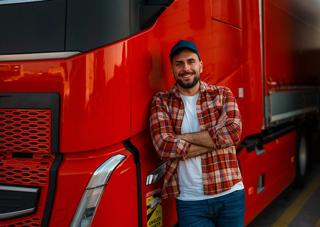 Flexible start up truck loans funded for a happy new owner-operator leaning with crossed arms against his red semi-truck