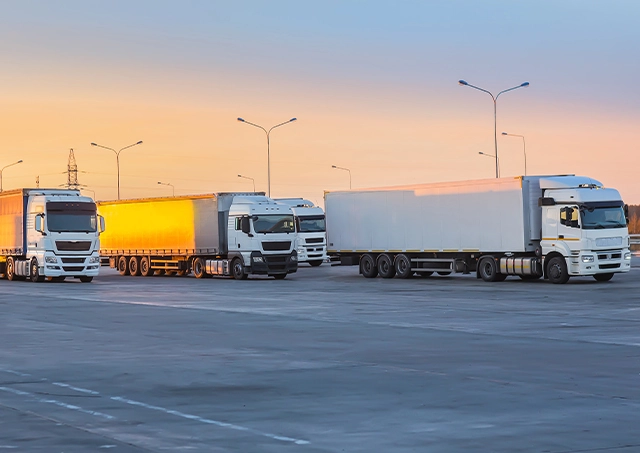 Trucks parked in a lot along a suburban highway at dawn.